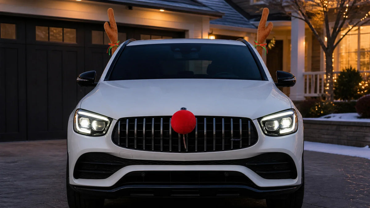 White SUV wearing plush reindeer antlers and a red Rudolph nose outside a decorated home