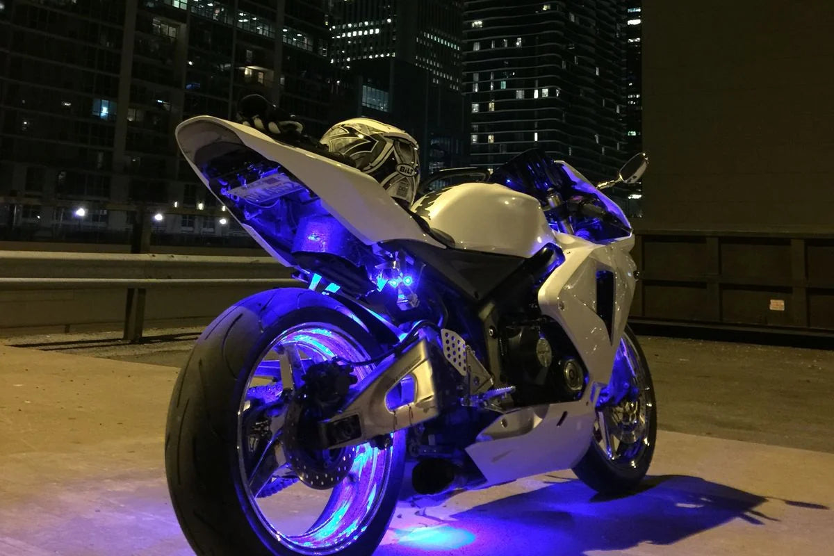 Blue rechargeable LED accent lights around a motorcycle frame and wheel area in a city night scene.