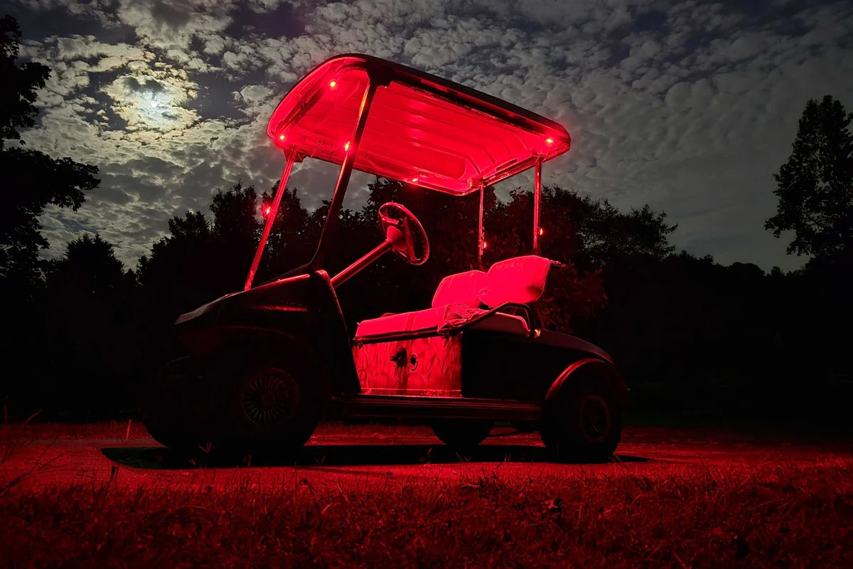 Red rechargeable LED accent lights adding a bold glow around a golf cart roof and cabin at night.