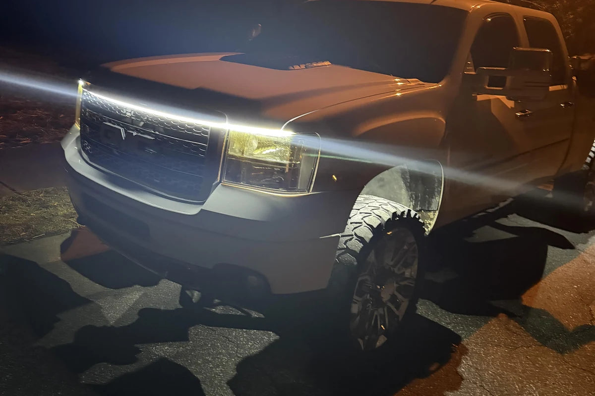 White truck hood LED light strip creating a continuous front-end glow on a dark roadside.